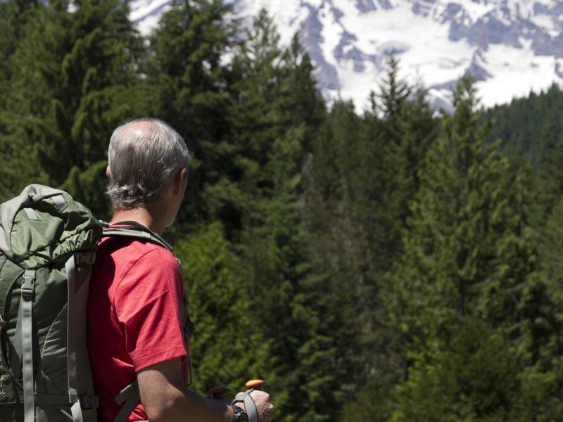一个背着背包的男人站在一条小路上望向雷尼尔山